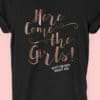 Image to buy product Here Come The Girls Glitter Personalised Hen Party T Shirt. Script lettering in glitter rose gold print with subtext in white on a black t-shirt.