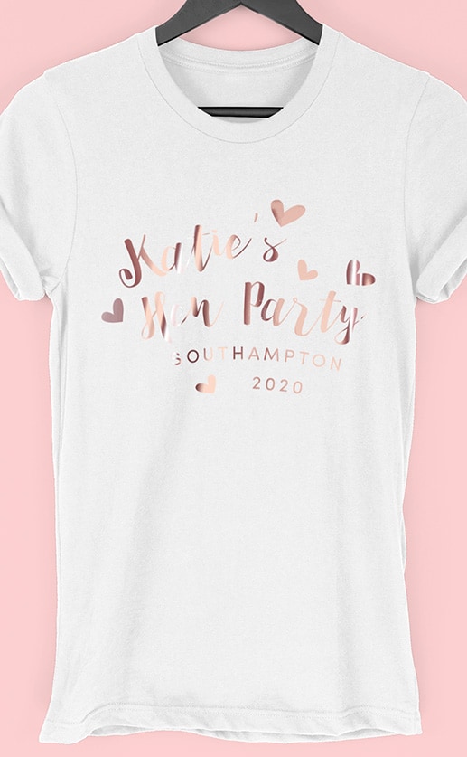 Image to buy product Love Hearts Personalised Hen Party T Shirt. Script lettering with love heart graphics in rose gold foil print on a white t-shirt.